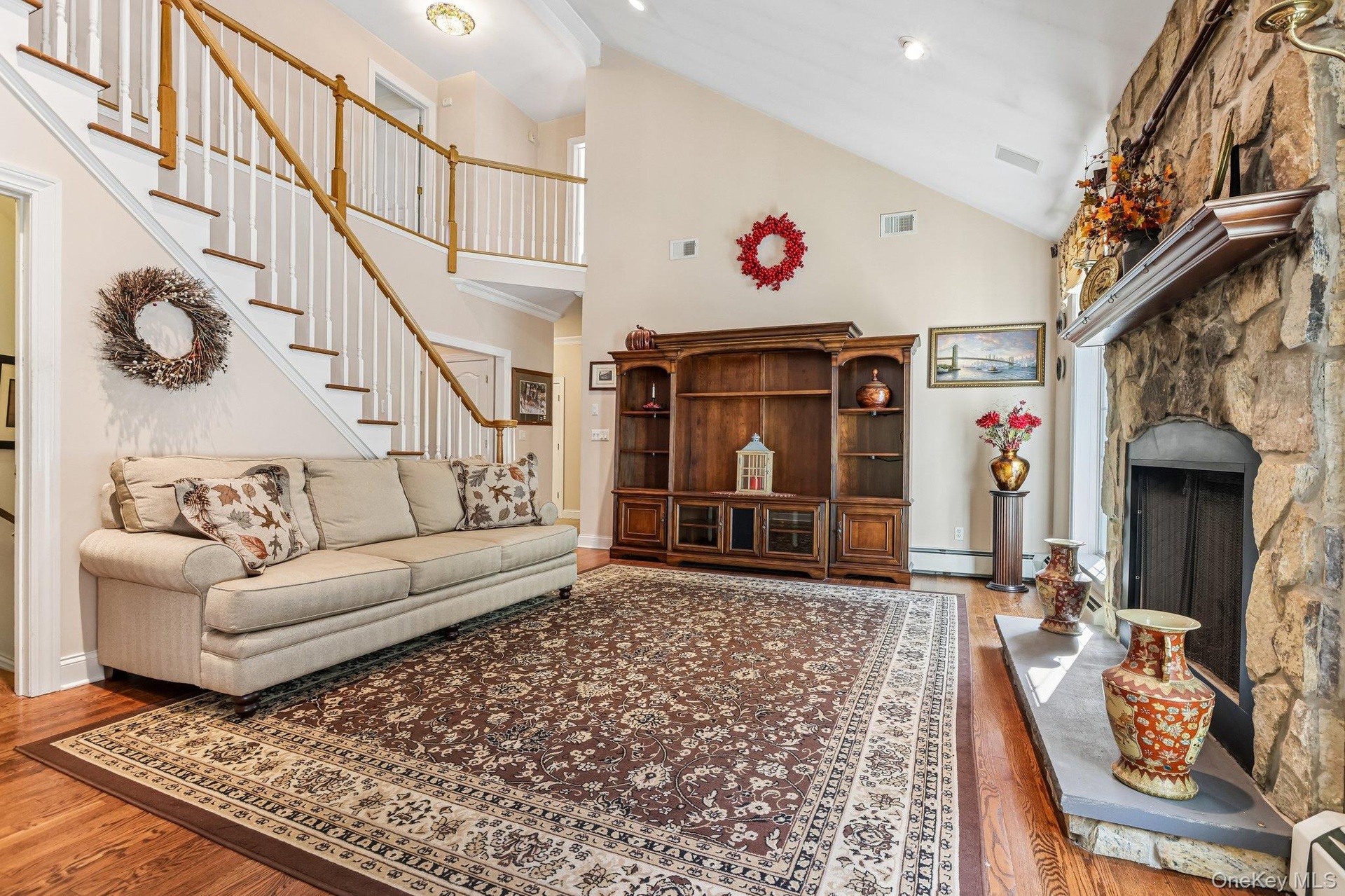 Stone fireplace with hearth, vaulted ceiling, wood-finish flooring, and a multi-level staircase with wood railings