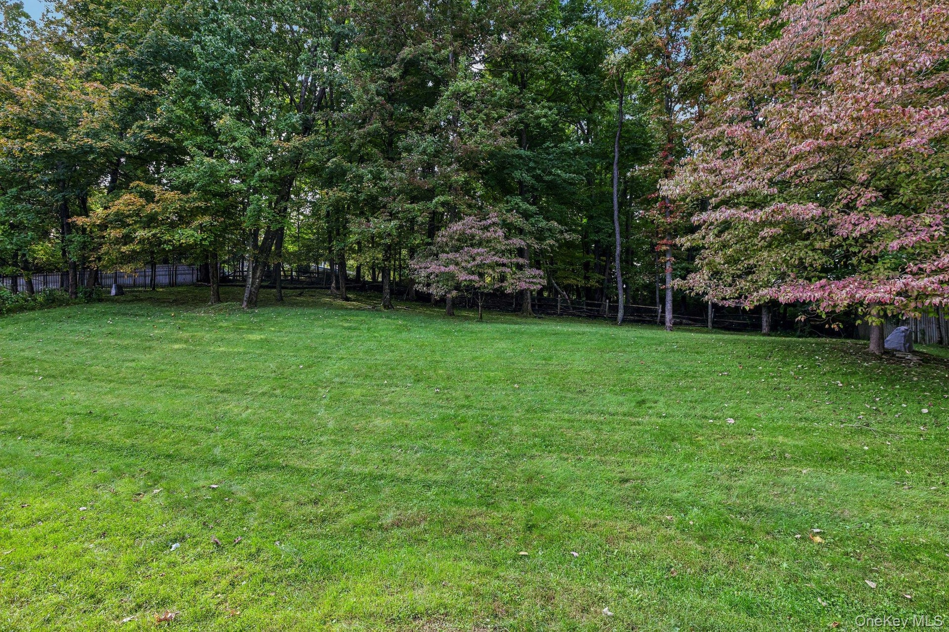 Expansive green lawn with mature trees and a partial wood fence