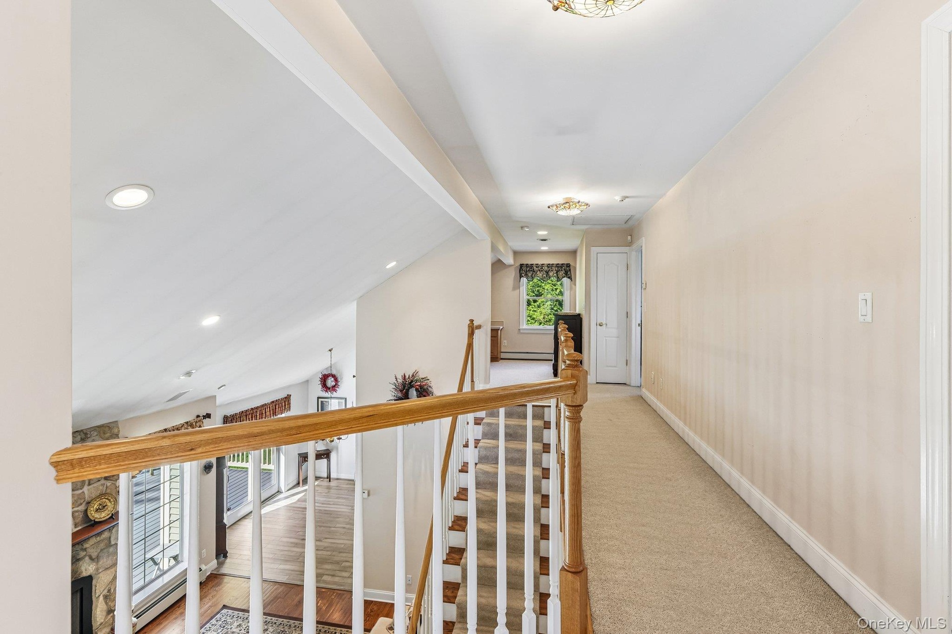 Carpeted hallway with flush-mount lighting, wood handrails, and white balusters