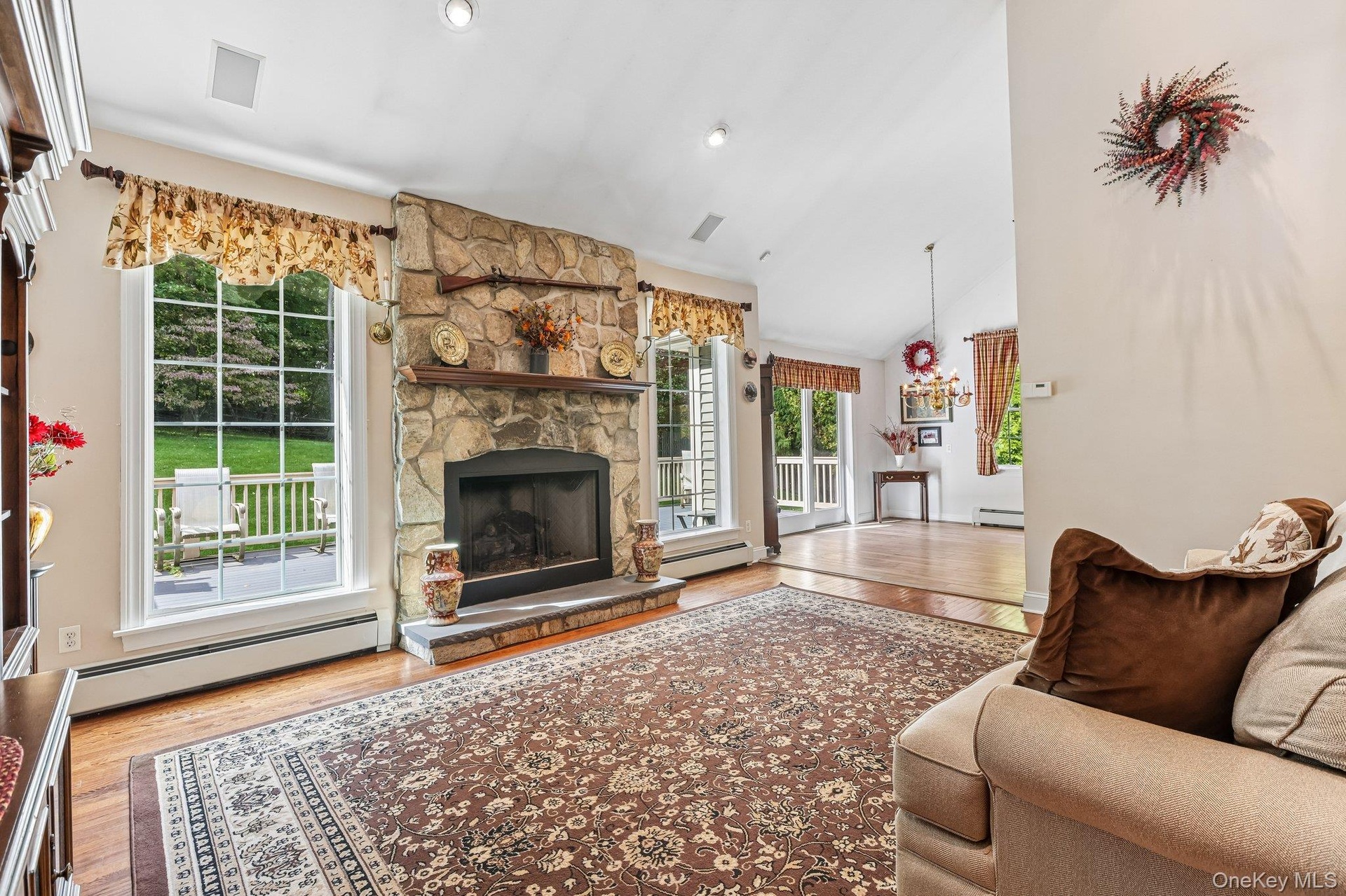 Vaulted ceiling with recessed lighting, stone fireplace with hearth and wood mantel, large pane windows, and wood-finish flooring
