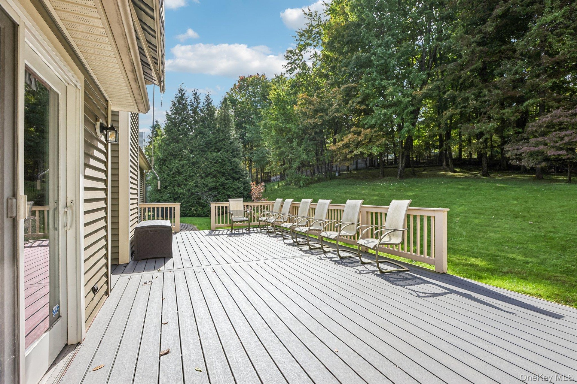 Expansive outdoor deck with railing, sliding glass door access, and a large manicured lawn surrounded by mature trees