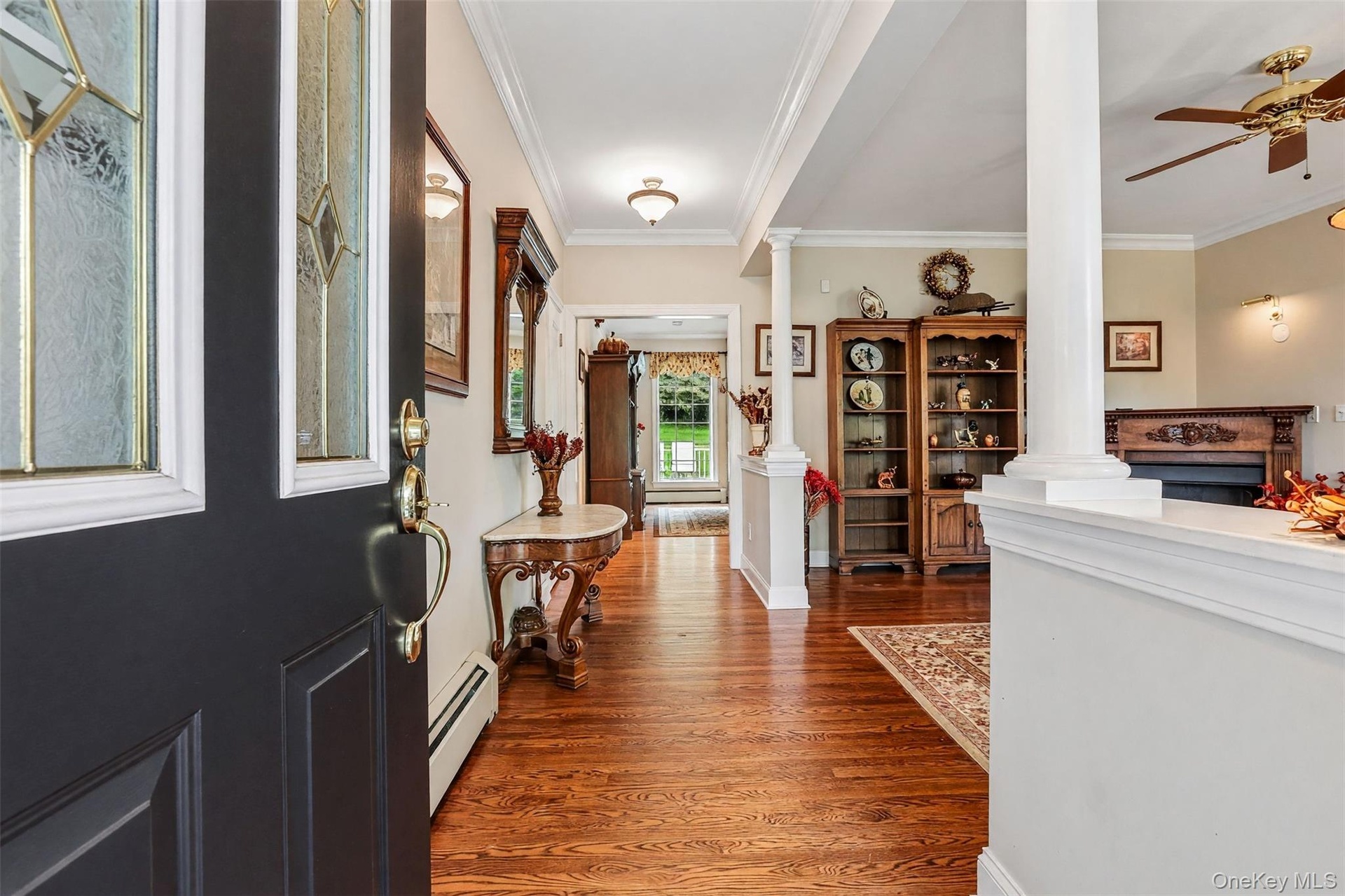 Hardwood flooring, decorative columns, crown molding, a built-in fireplace, and a ceiling fan