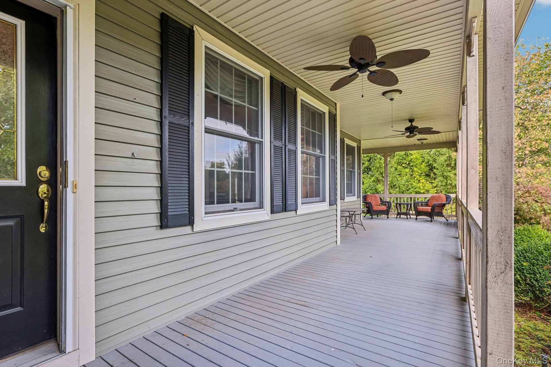 Expansive covered porch featuring ceiling fans, light-toned siding, and dark window shutters