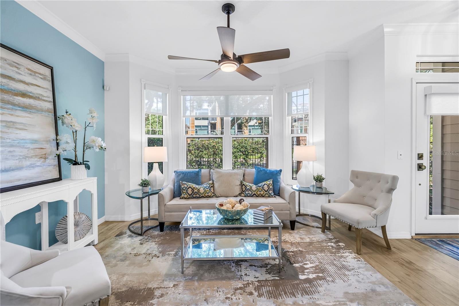 Bright and inviting living room features a bay window, luxury vinyl plank flooring and a remote-controlled sun shade.