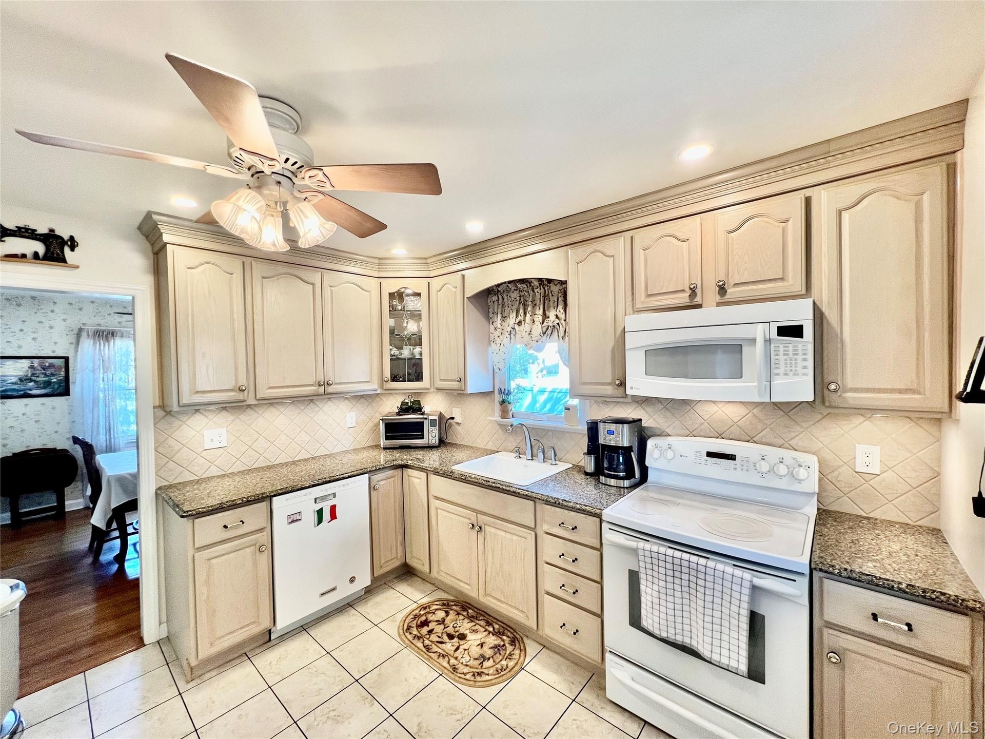 Kitchen featuring light-toned cabinetry, a ceiling fan with integrated lighting, a tile backsplash, and a built-in microwave