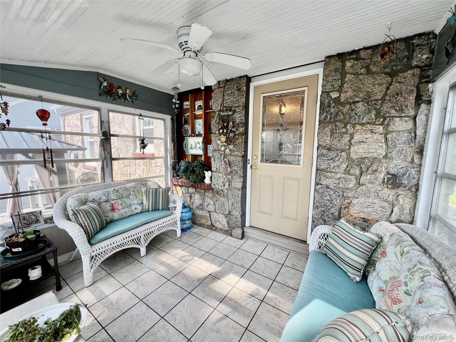 Enclosed porch featuring exposed stone walls, tiled flooring, multiple windows, a ceiling fan, and a door with decorative glass