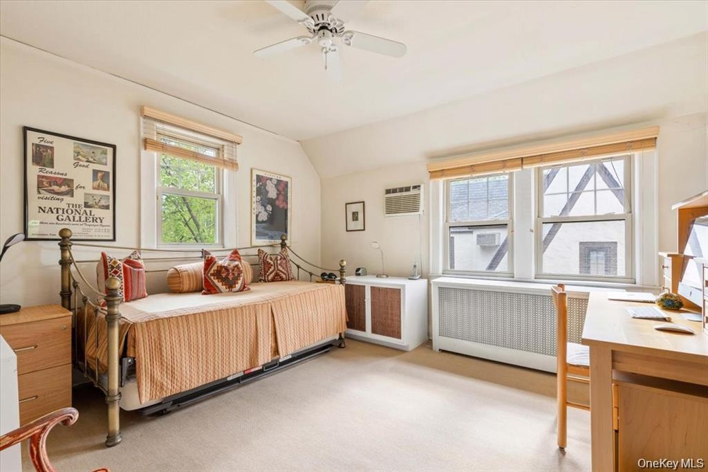 Bedroom featuring radiator, light colored carpet, lofted ceiling, a wall mounted AC, and a ceiling fan