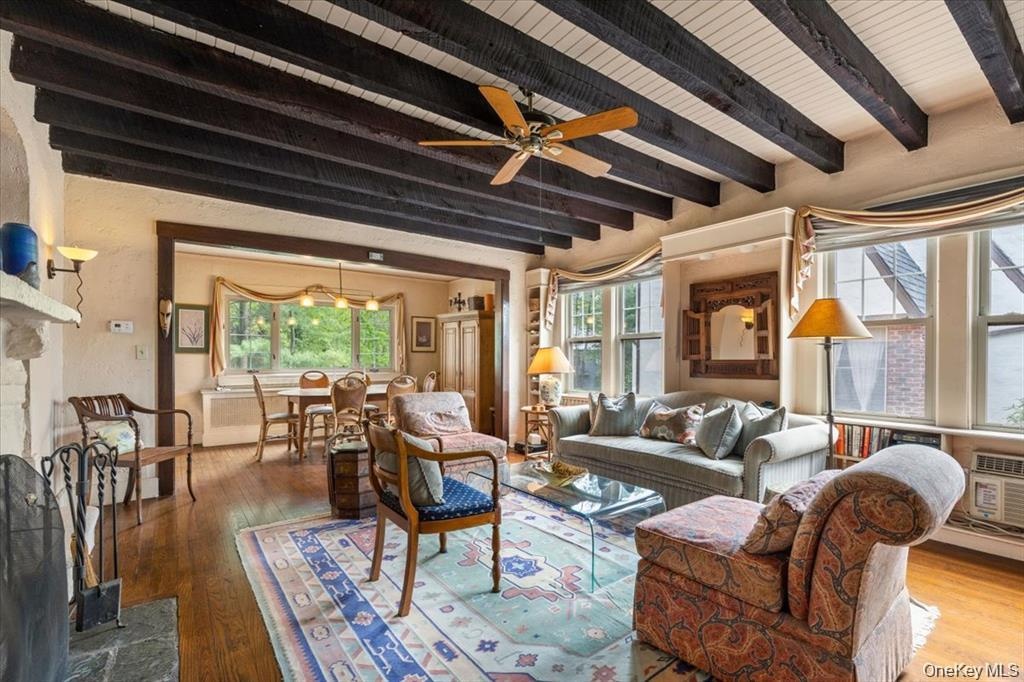Living room with beam ceiling, healthy amount of natural light, wood-type flooring, and ceiling fan