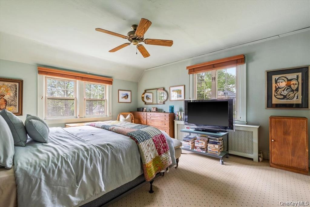 Carpeted bedroom with vaulted ceiling, radiator heating unit, and ceiling fan