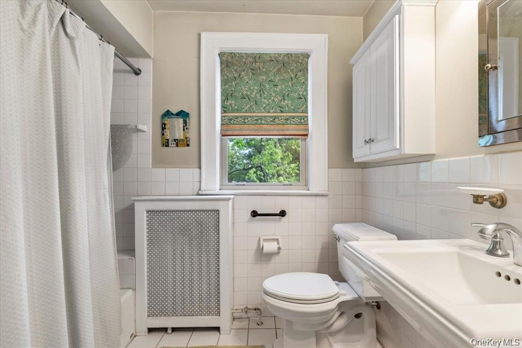 Full bathroom with tile walls, radiator heating unit, toilet, tile patterned flooring, and shower / bath combo