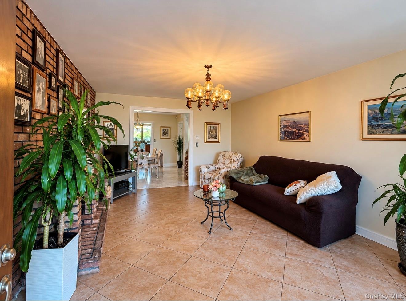 Tiled flooring throughout, brick accent wall, and a multi-bulb chandelier