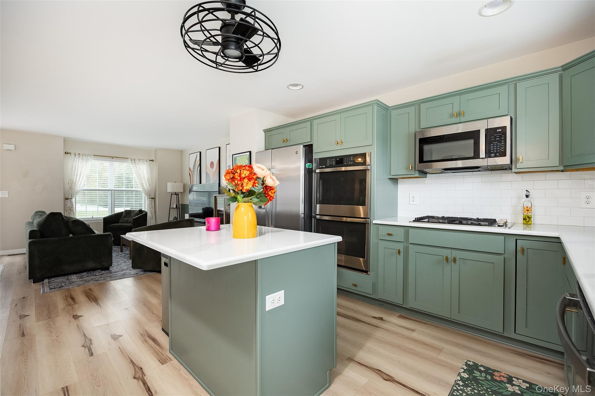 Open-concept kitchen with sage green cabinetry, stainless steel appliances, white subway tile backsplash, and a central island with a white countertop