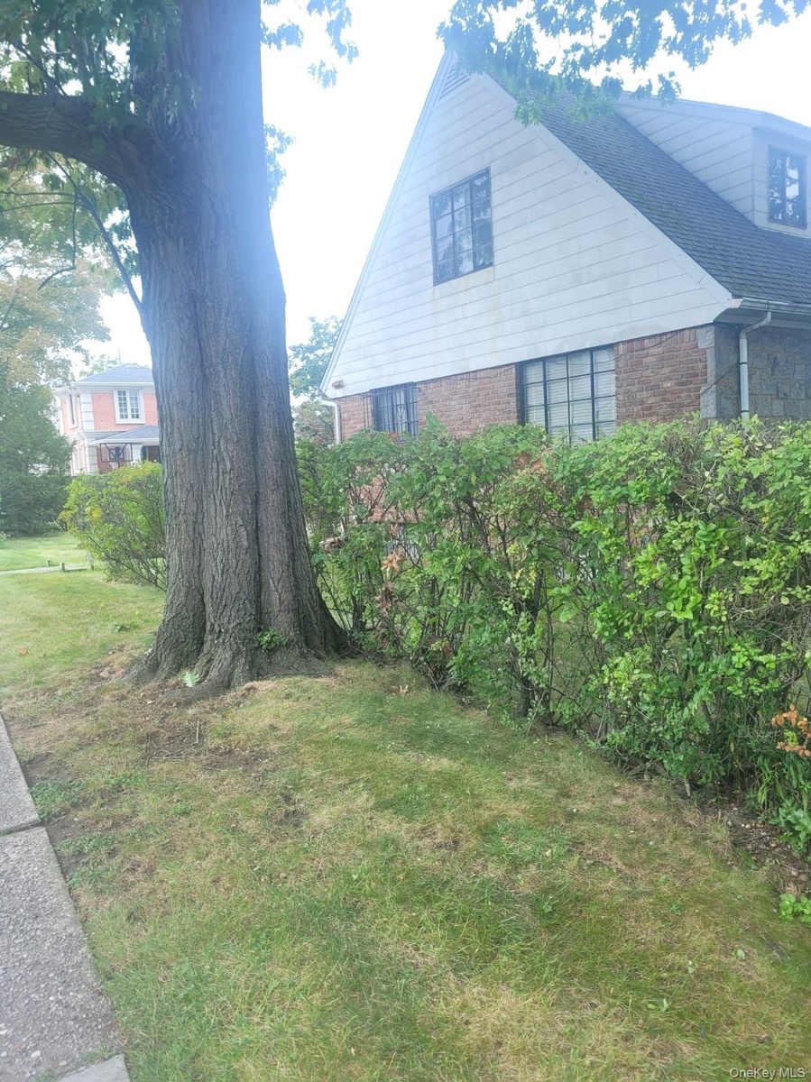 Gable roofline with dormer window, brick and siding exterior, established tree, and sidewalk access