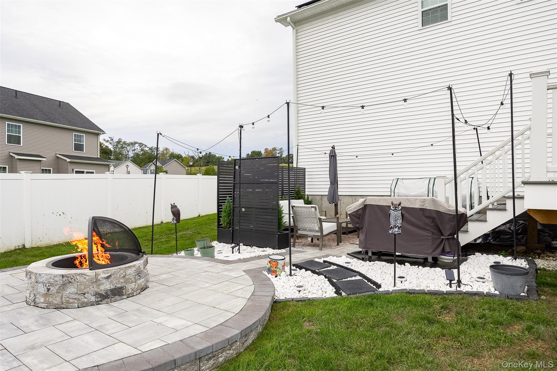 Paver patio with a stone fire pit, string lights, and a white privacy fence