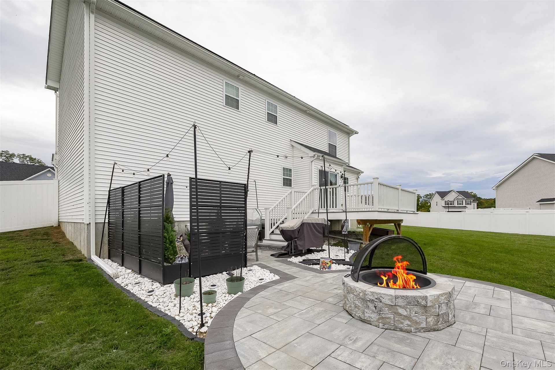 Backyard patio featuring a stone-finish fire pit, paver hardscaping, and a white privacy fence