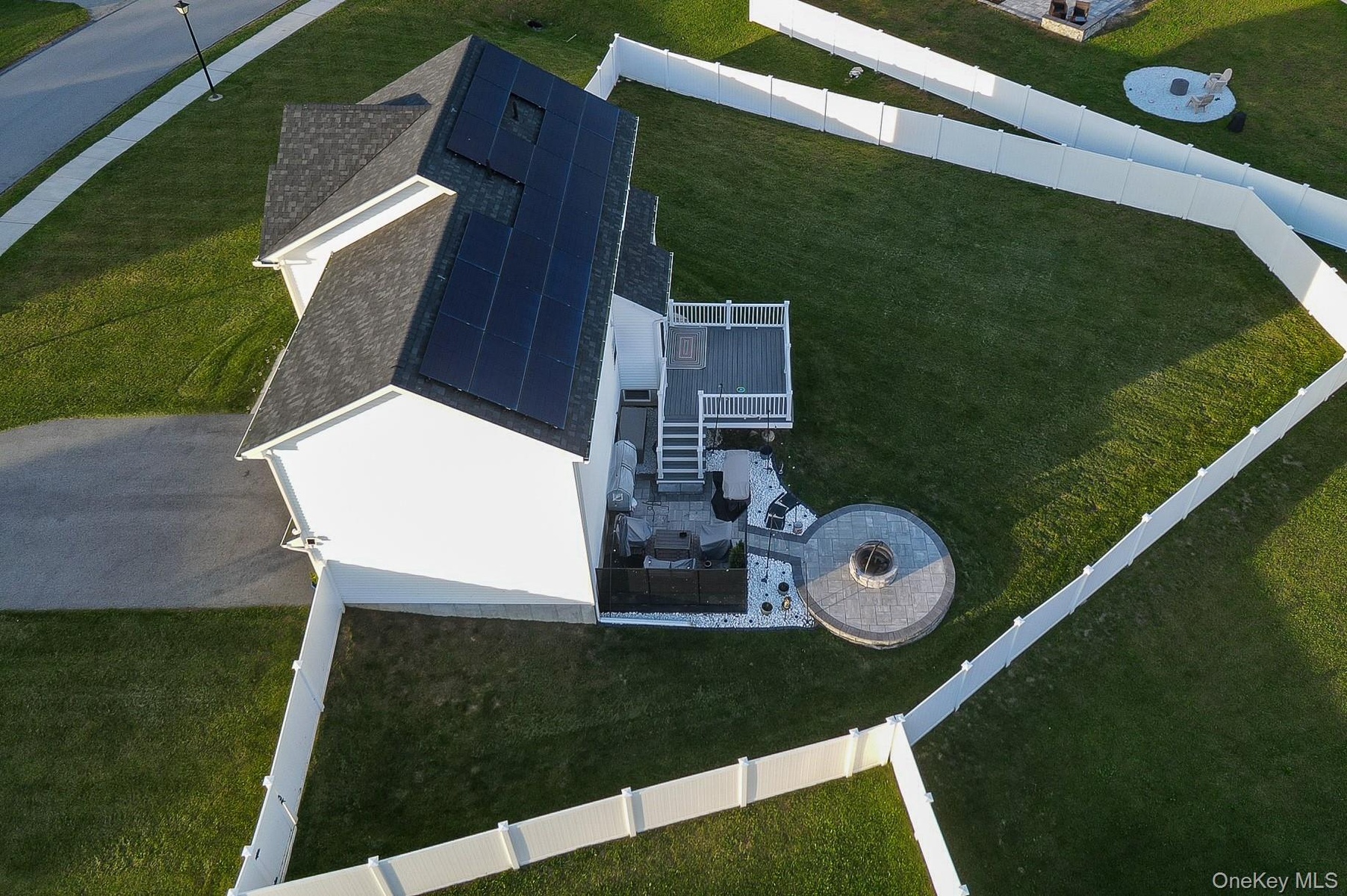 White exterior with a dark shingle roof, solar panel array, and a composite deck