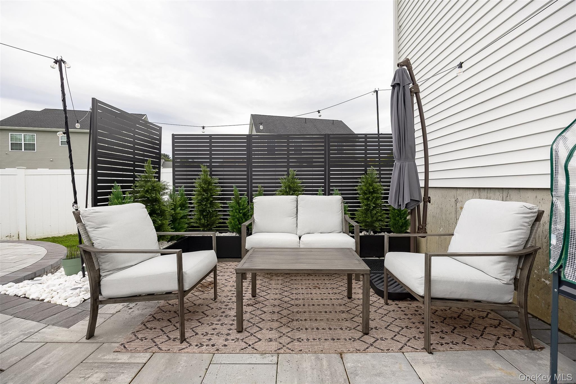 Paver patio with a circular inlay, white siding, and privacy screens