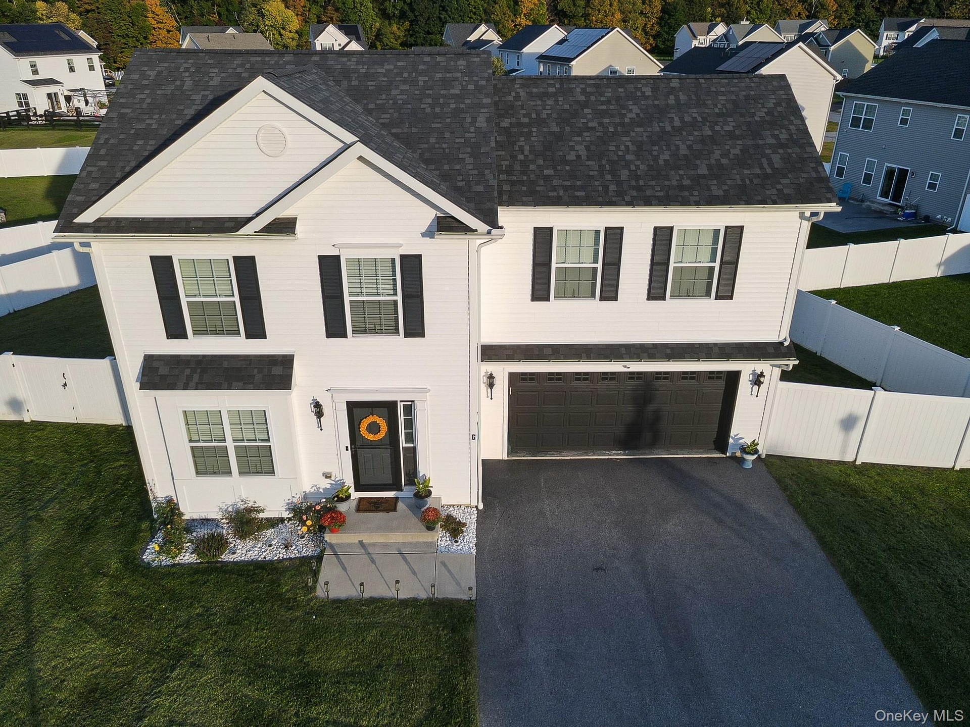 White siding with black shutters, dark shingle roof, two-car garage, paved driveway, and a white picket fence
