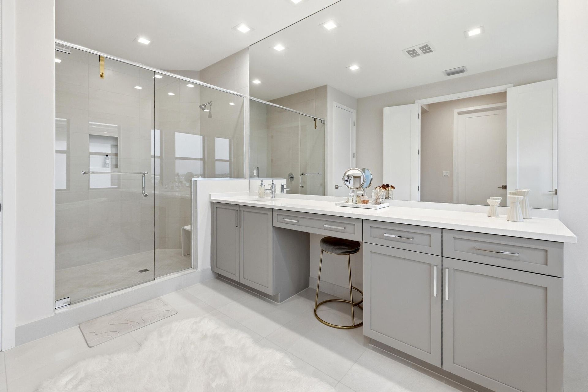 Spacious bathroom featuring a frameless glass shower enclosure, a full-width vanity mirror, light-toned tile flooring, recessed lighting, and gray sha