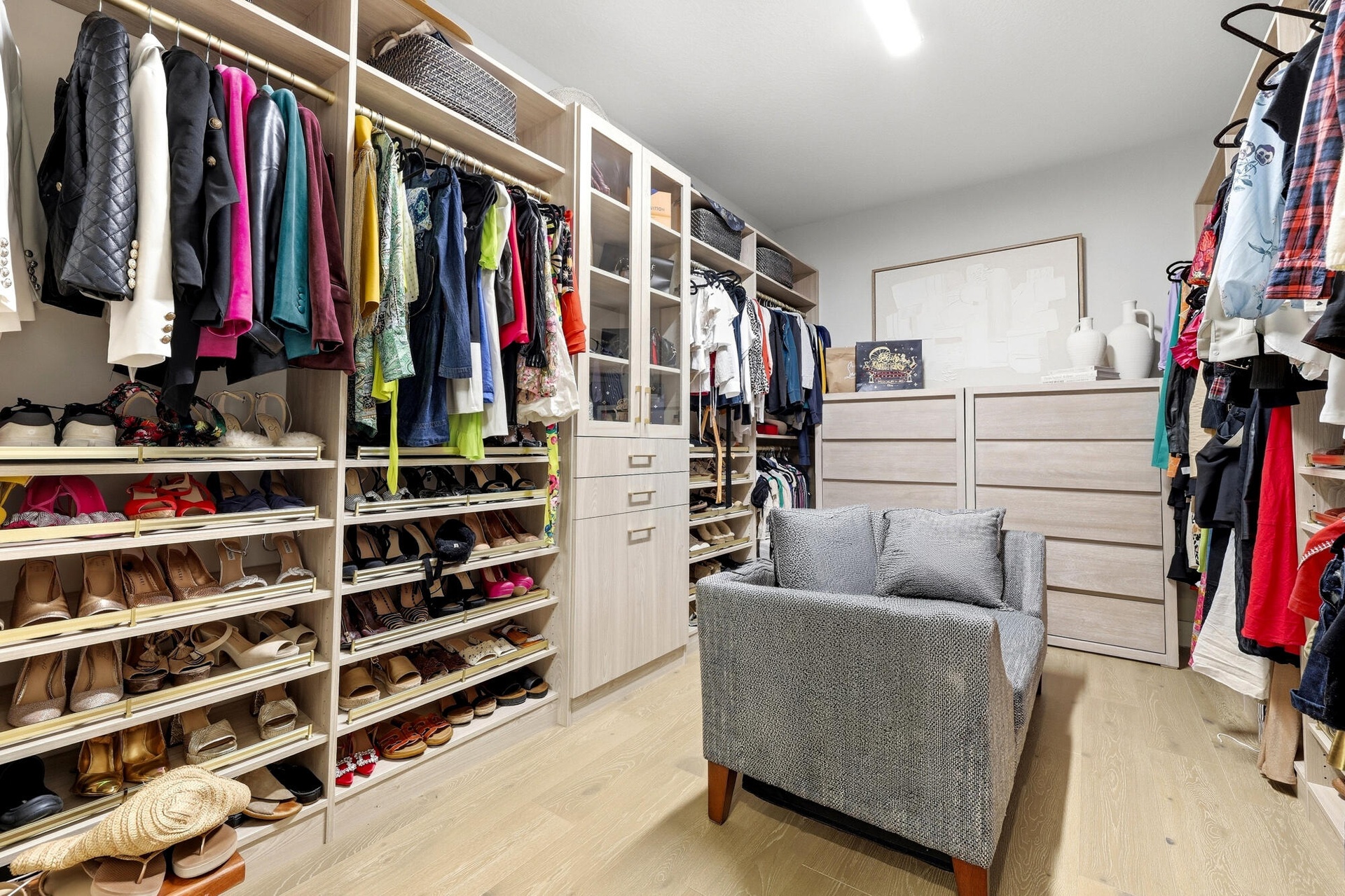 Custom closet system with extensive shelving, multiple hanging rods, built-in drawer storage, and glass-front cabinetry