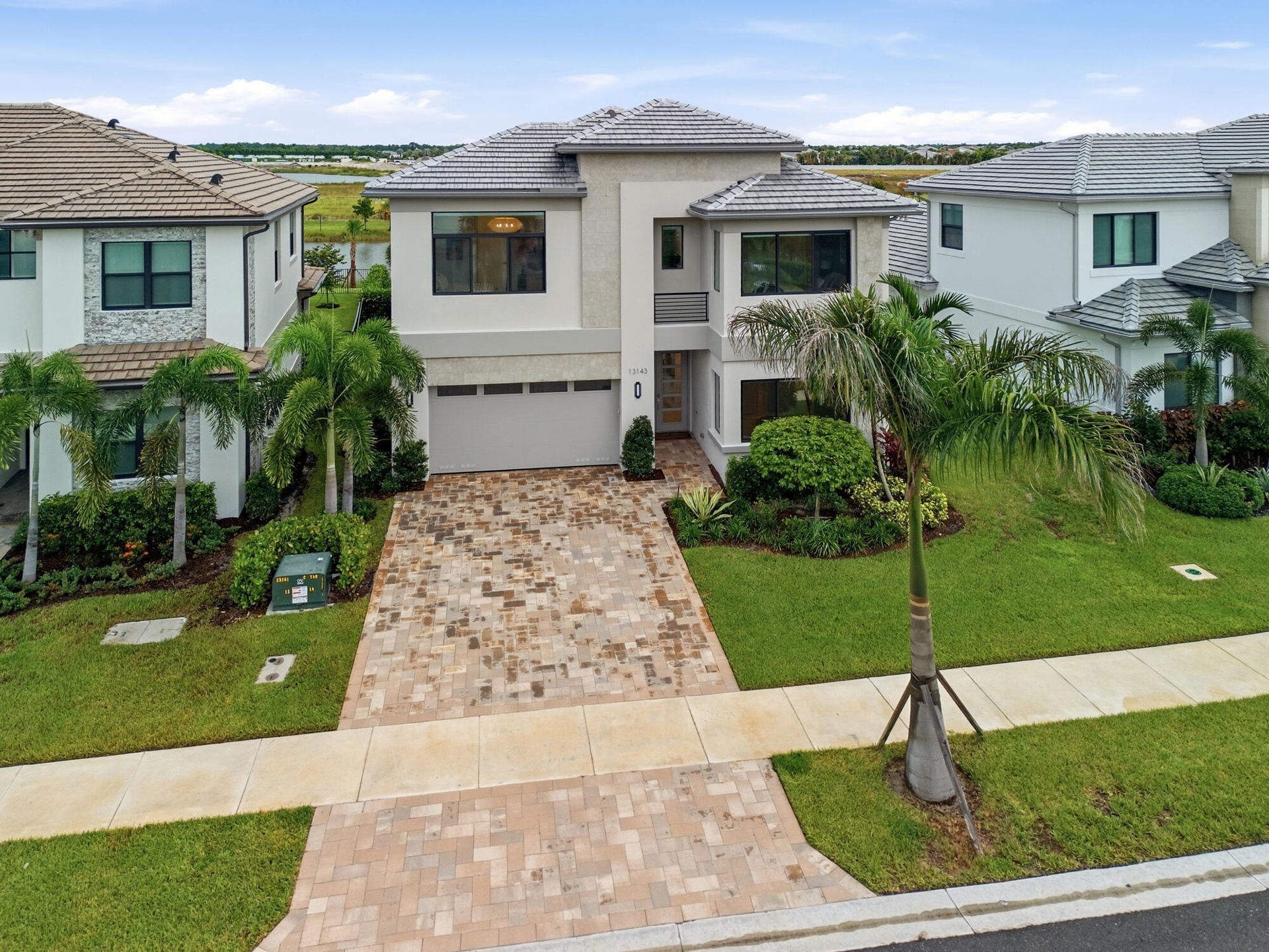 Modern stucco exterior with decorative stone accents, a paver driveway, and a tile roof
