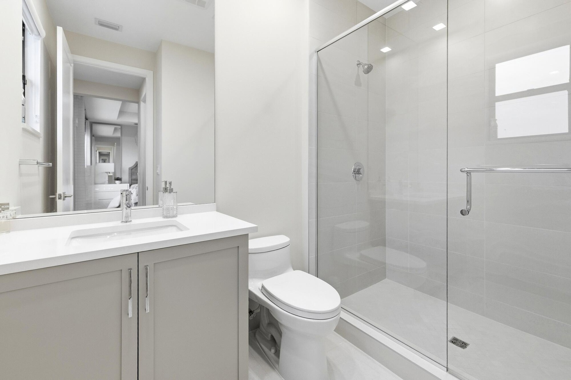 Contemporary bathroom featuring a single vanity with light grey cabinetry, a rectangular undermount sink, and a glass-enclosed shower with a chrome sh