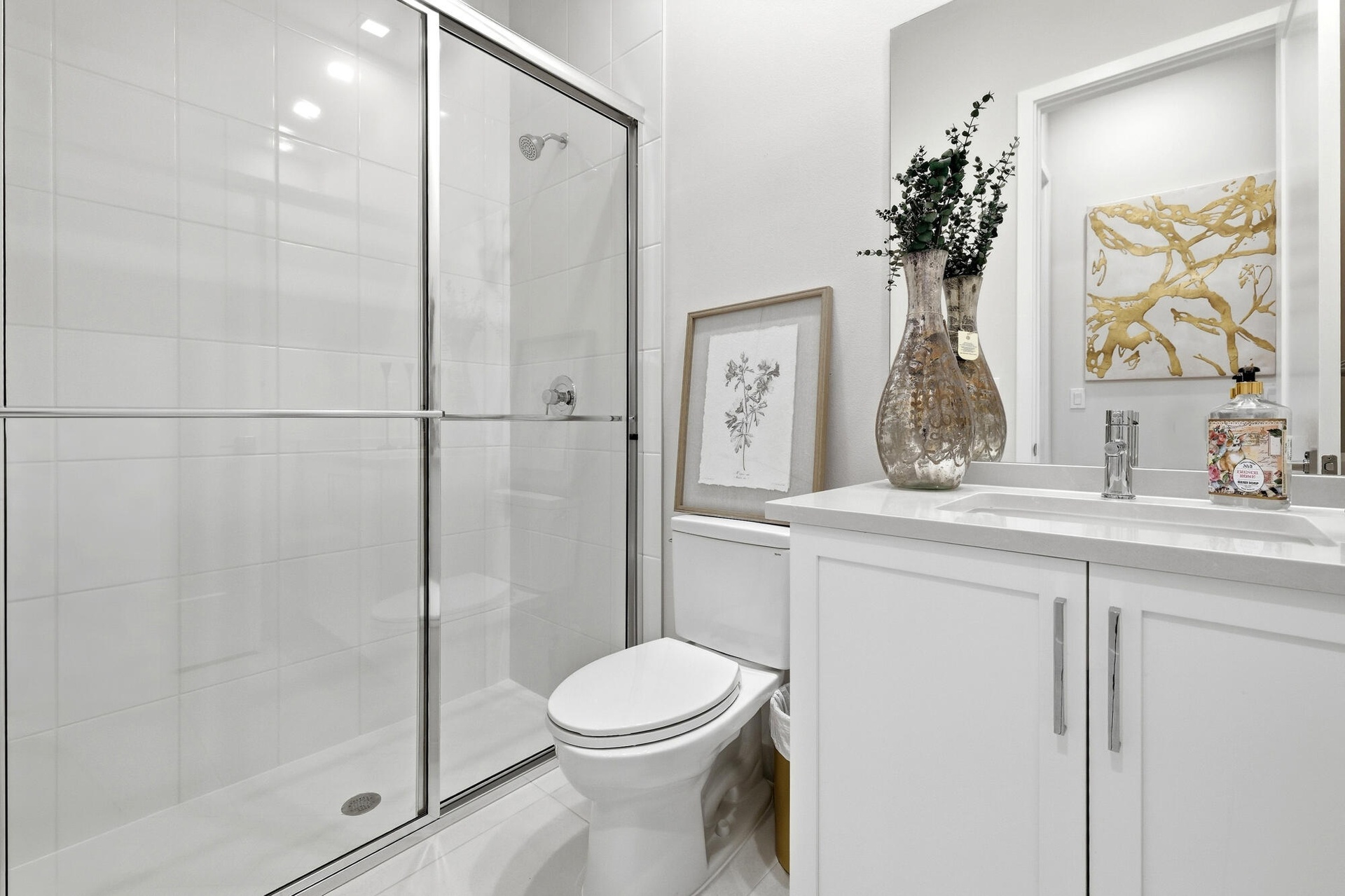 Shower with sliding glass doors, white tiled walls, white vanity with integrated sink, chrome faucet, and white cabinetry