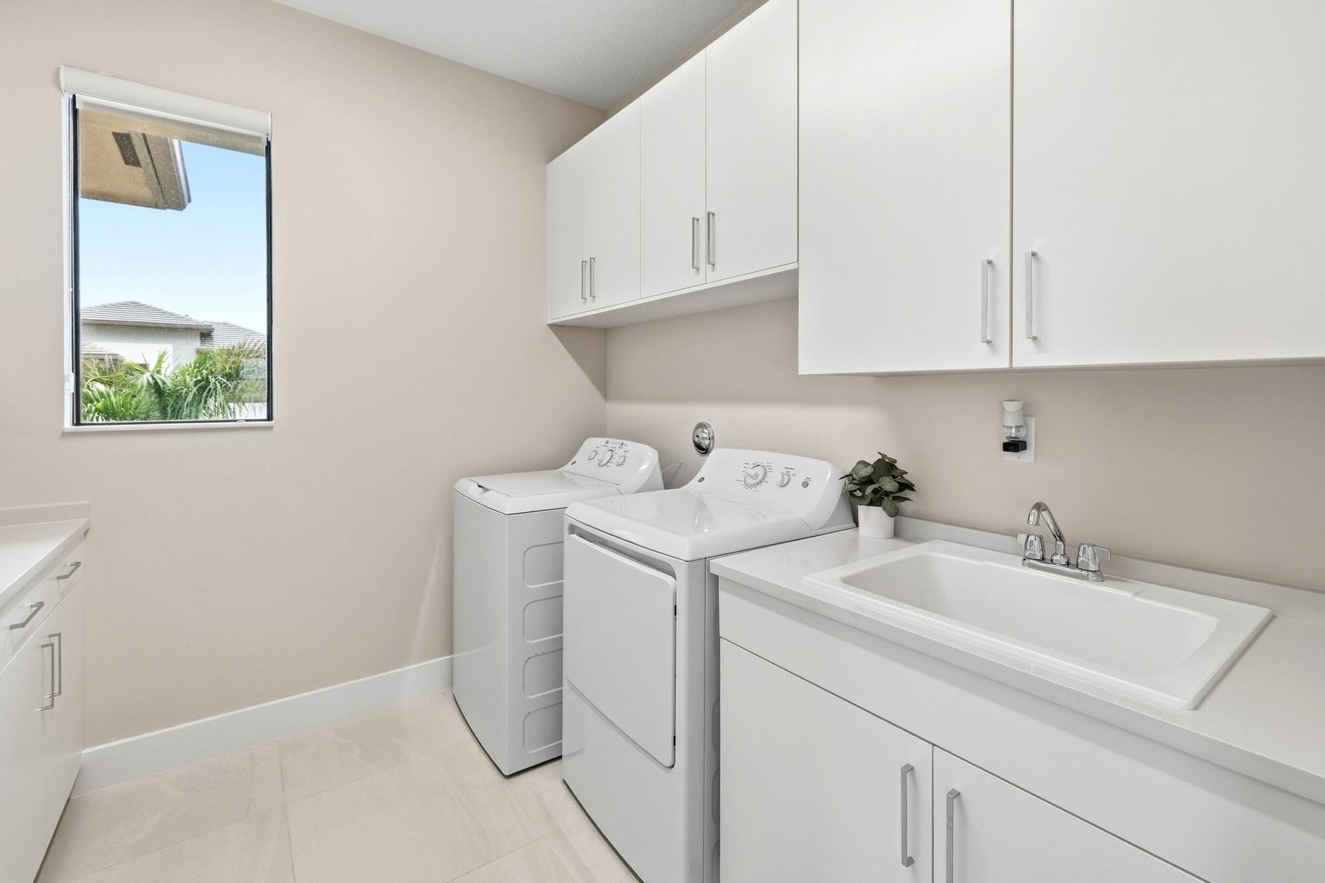 White shaker-style cabinetry with chrome hardware, an integrated laundry sink, light-toned countertop, and light-colored tile flooring