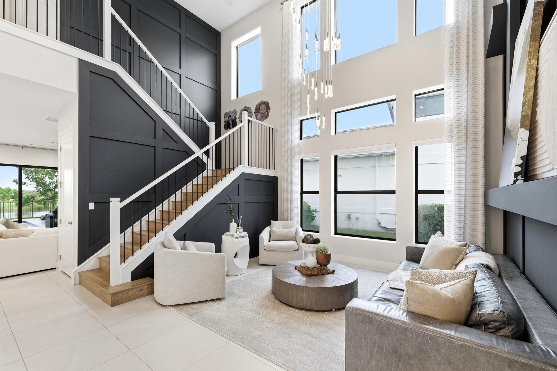 Two-story living area with high ceilings, multiple large windows, a built-in shelving unit, and a prominent staircase with wood-finish treads and an o