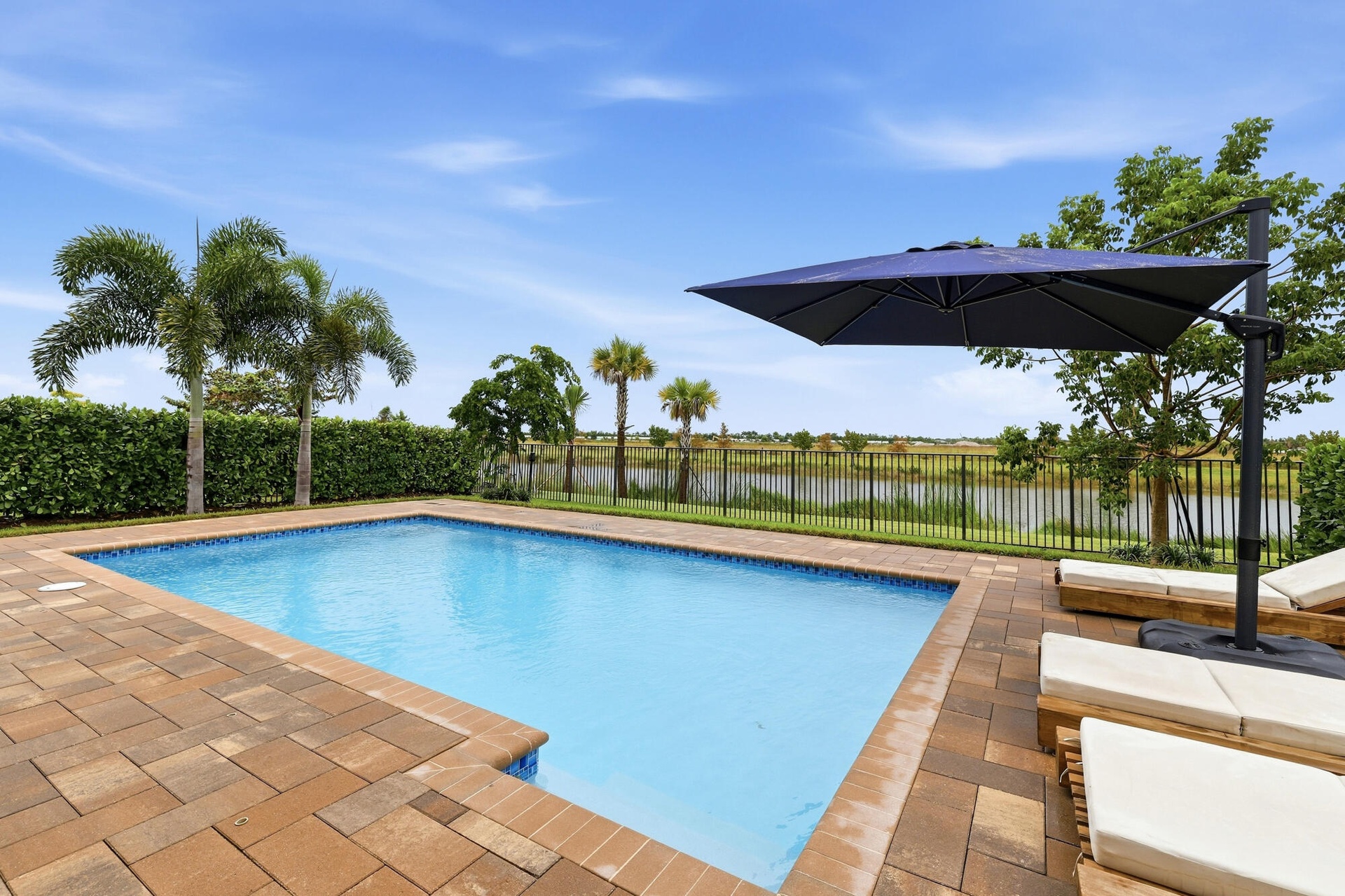 Rectangular swimming pool with paver decking, enclosed by a black metal fence, overlooking a body of water