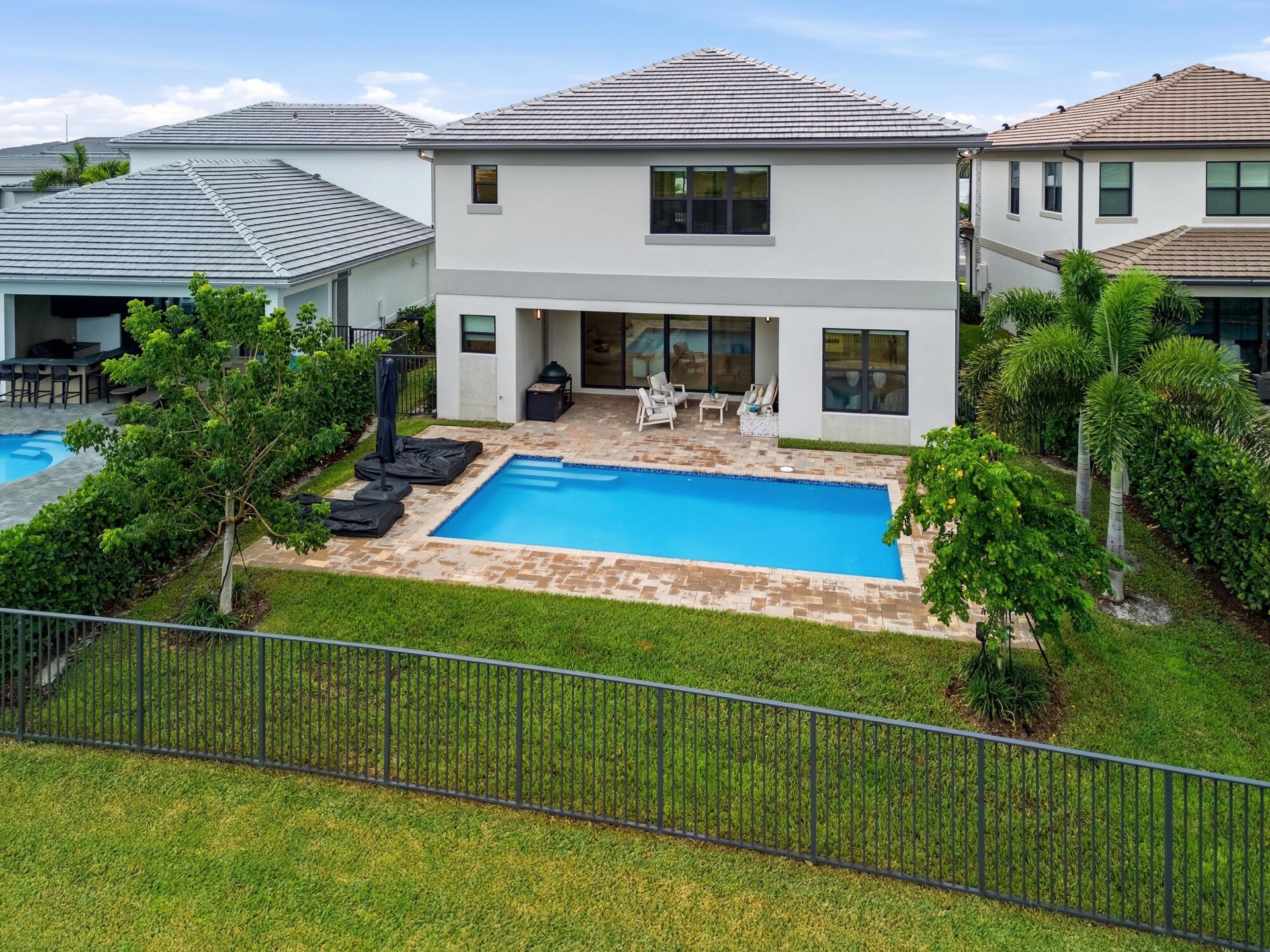 Two-story stucco exterior with a tile roof, featuring a private swimming pool, paver patio, and a fenced lawn