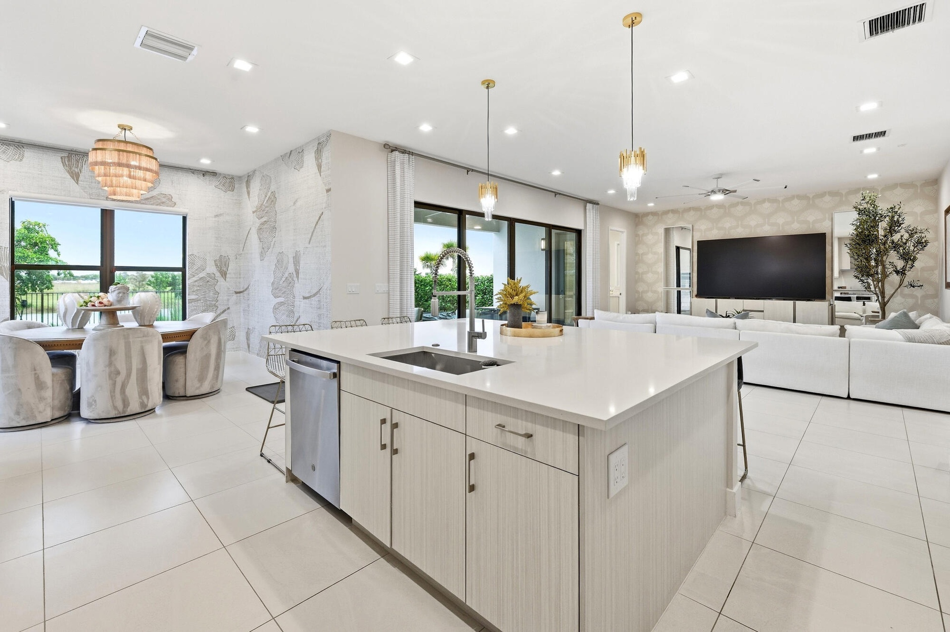 Open-concept interior featuring large format tile flooring, a kitchen island with sink and integrated dishwasher, and a dining area with expansive win
