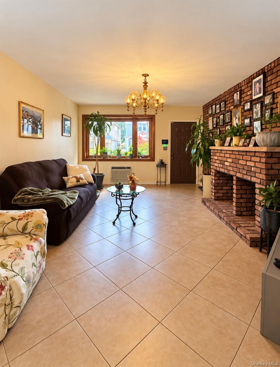Spacious living area featuring tile flooring, a prominent brick-clad fireplace, and a decorative chandelier