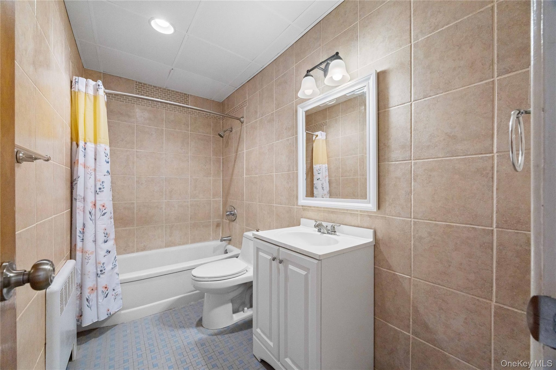 Full tile surround, white vanity, integrated sink, mirrored cabinet, and recessed ceiling lighting