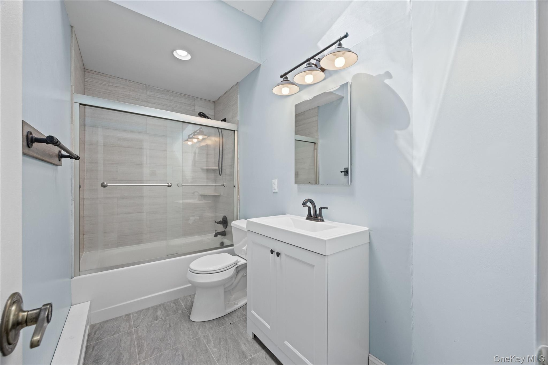 Sliding glass shower enclosure, white vanity with integrated sink, rectangular mirror, three-light vanity fixture, and recessed ceiling lighting