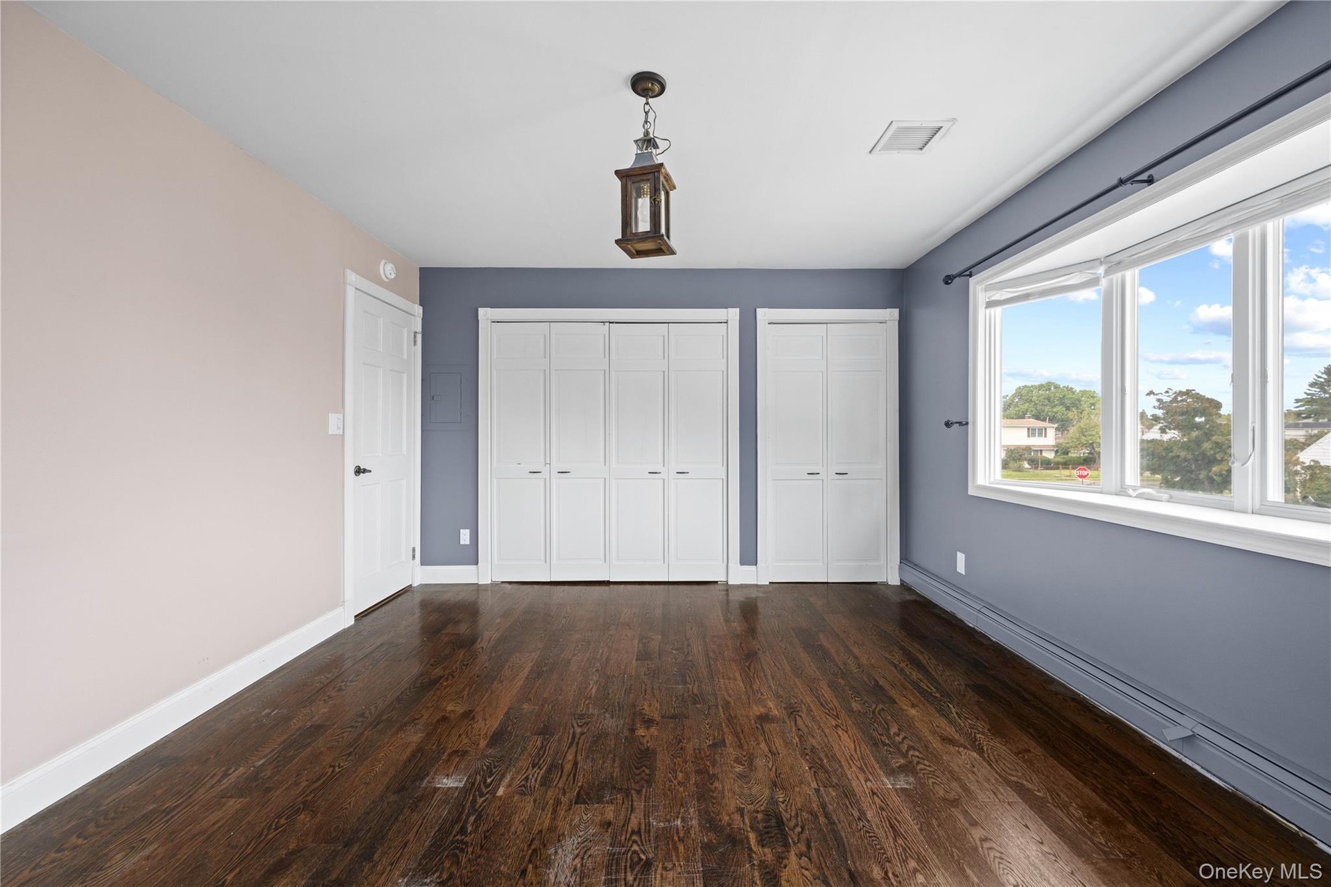 Dark wood-finish flooring, a decorative ceiling light fixture, and a bay window