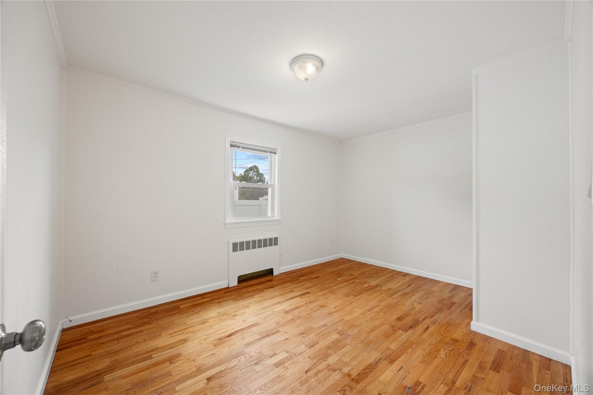 Wood-finish flooring, white painted walls, single window, baseboard heating unit, and ceiling-mounted light fixture
