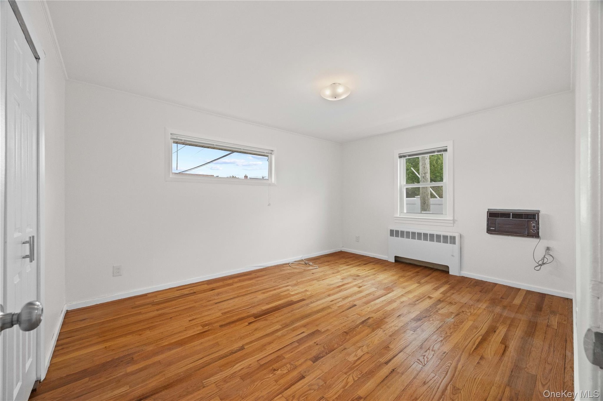Hardwood flooring, white painted walls, two windows, and a flush mount ceiling light