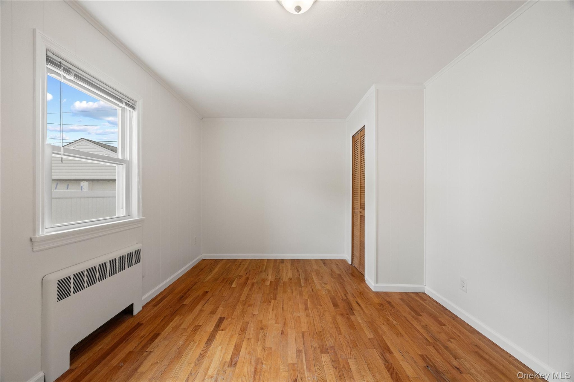Hardwood flooring, painted white walls, white window trim, white crown molding, and a wood-finish bi-fold door