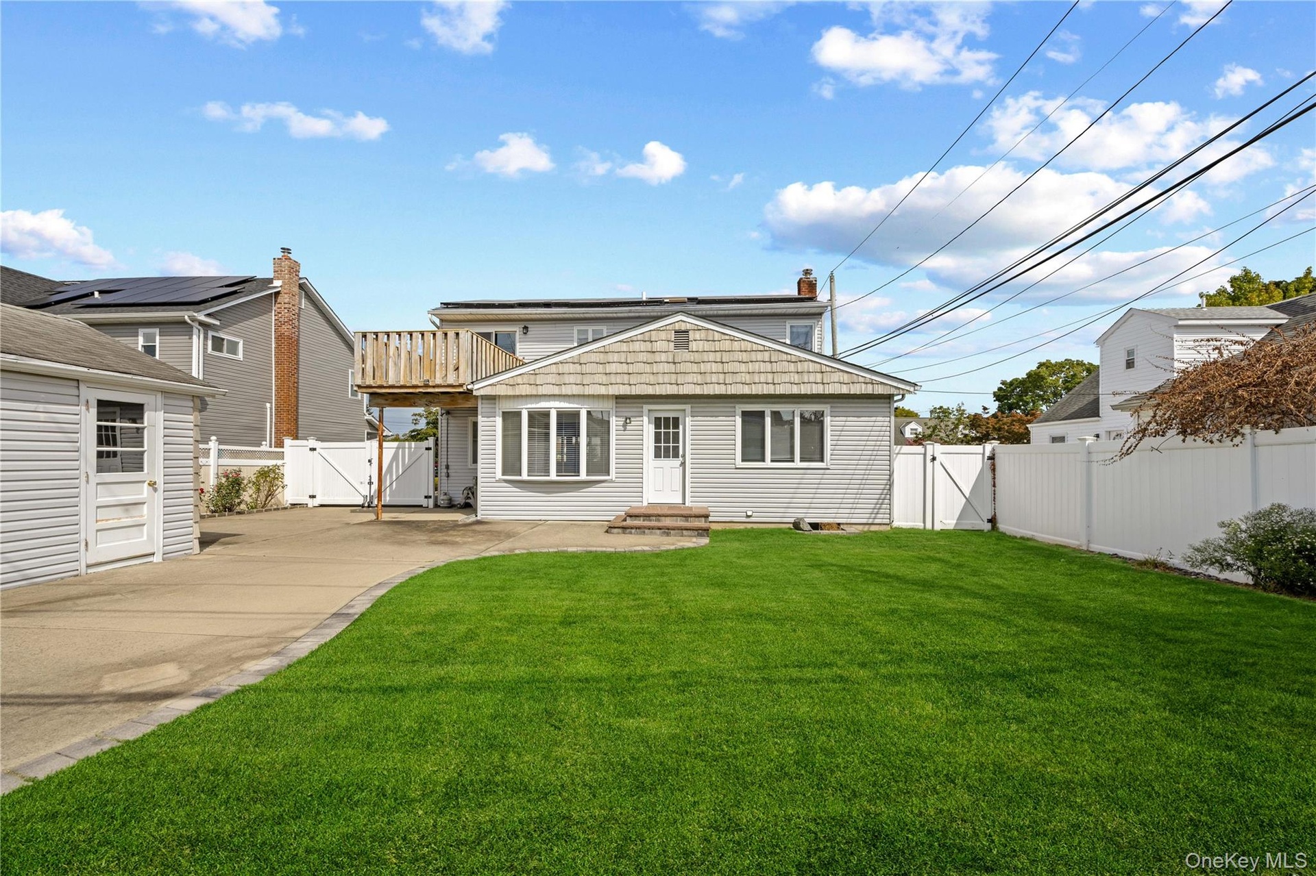 Expansive green lawn, white privacy fencing, paved driveway, detached garage, and a wood deck