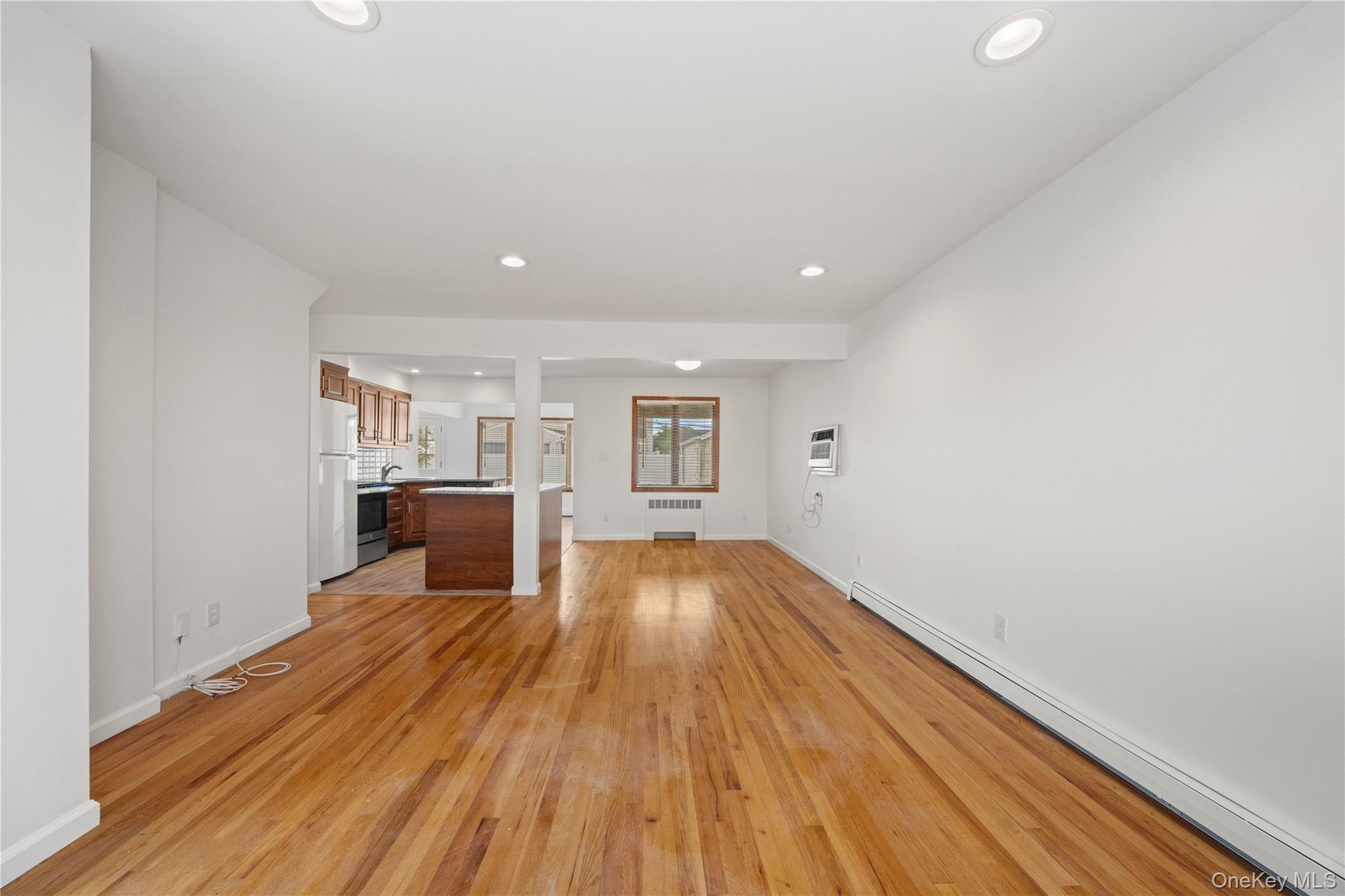 Wood-finish flooring throughout, recessed ceiling lighting, and a kitchen with wood cabinetry and a white refrigerator
