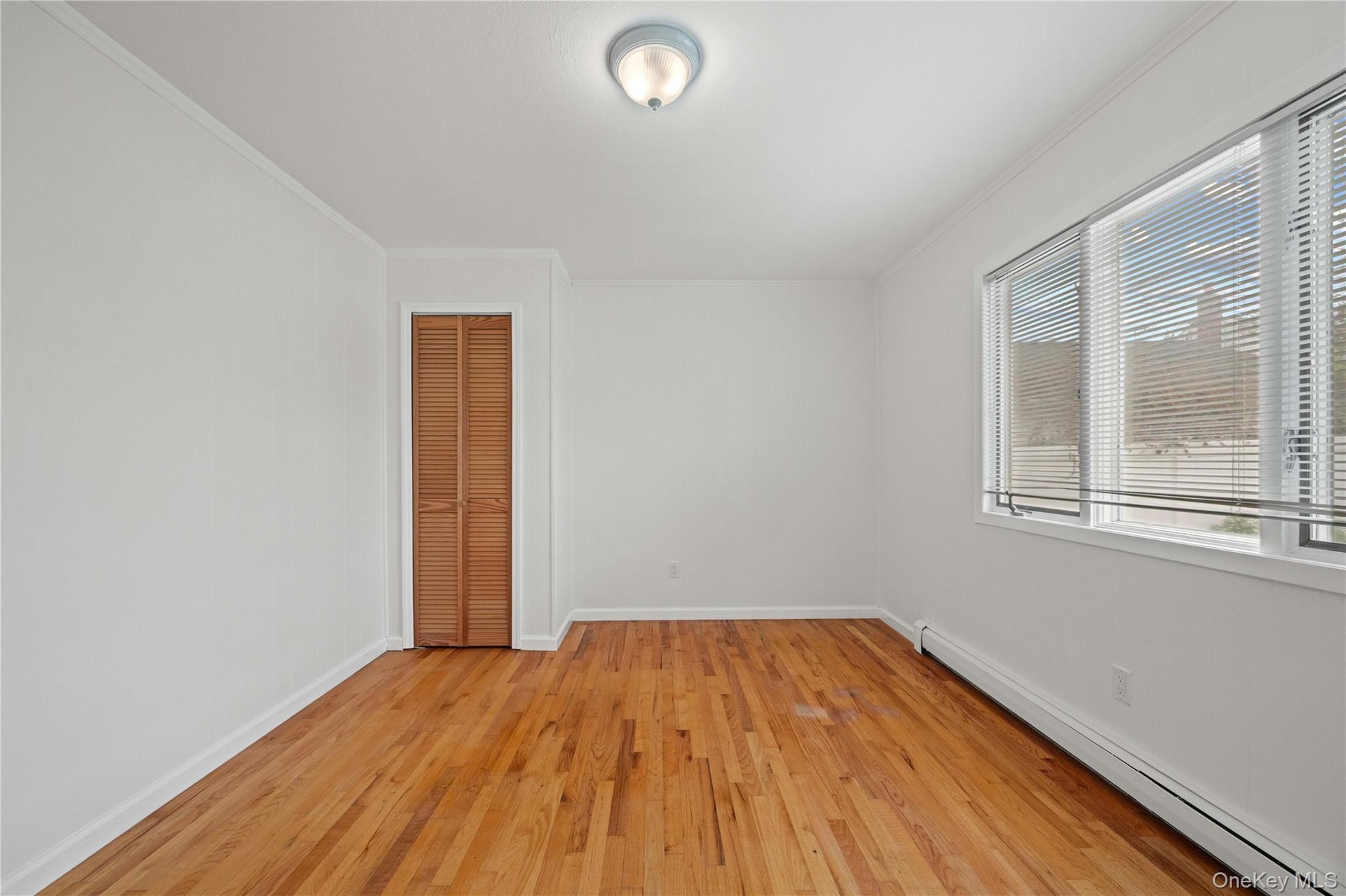 Hardwood flooring, painted walls, louvered closet doors, window with blinds, and ceiling-mounted light fixture