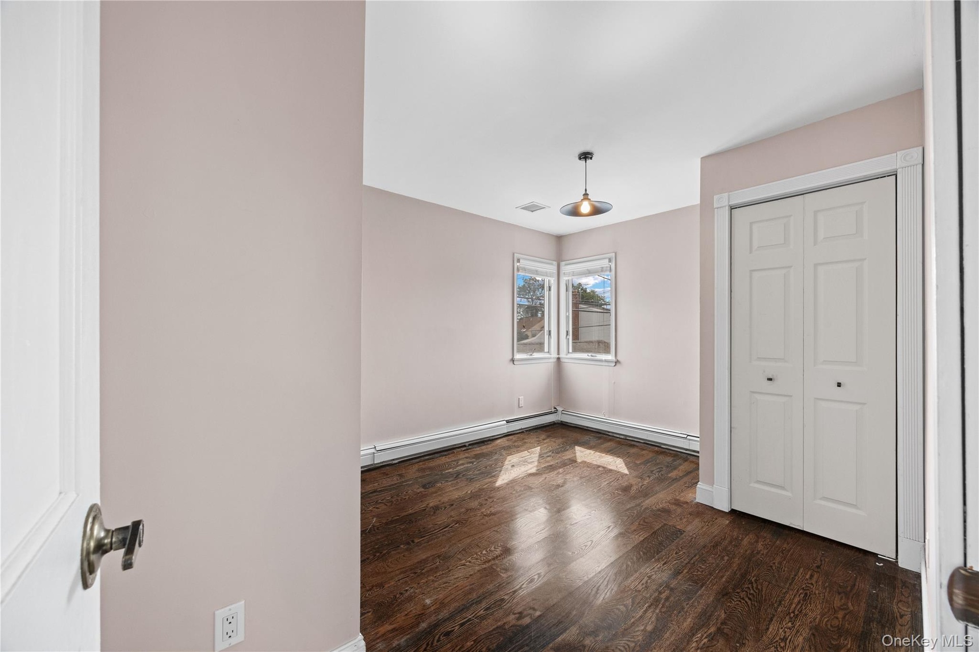 Hardwood flooring with a corner window, bi-fold closet doors, and a ceiling-mounted light fixture