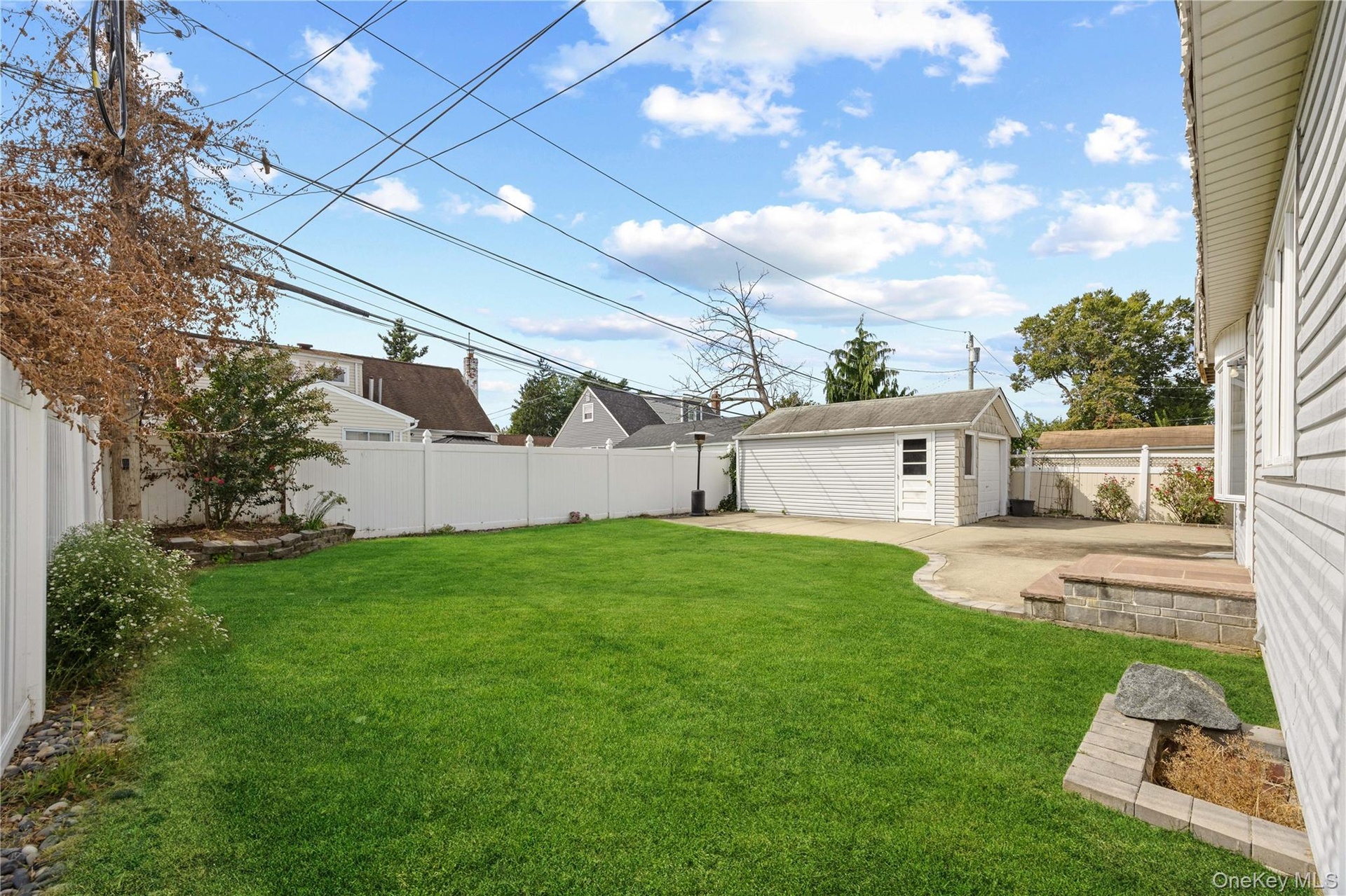Expansive lawn with a white privacy fence, detached garage, concrete patio, and stone landscape borders