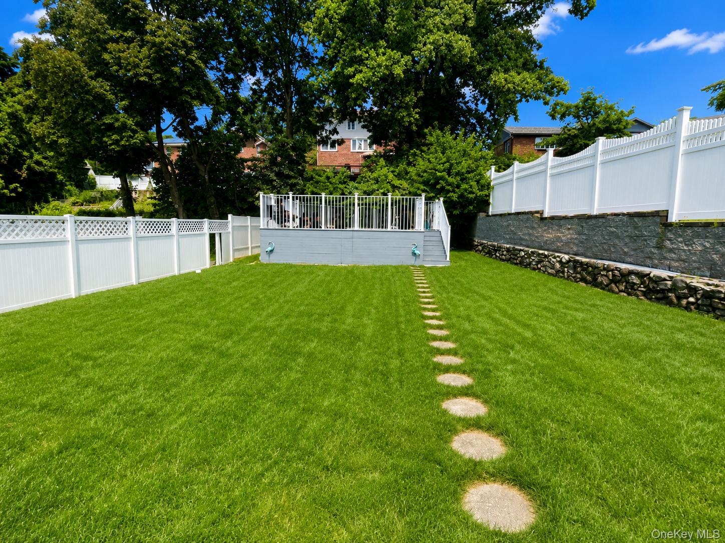 Expansive lawn with stepping stone pathway, white privacy fencing, and a raised composite deck with white railings