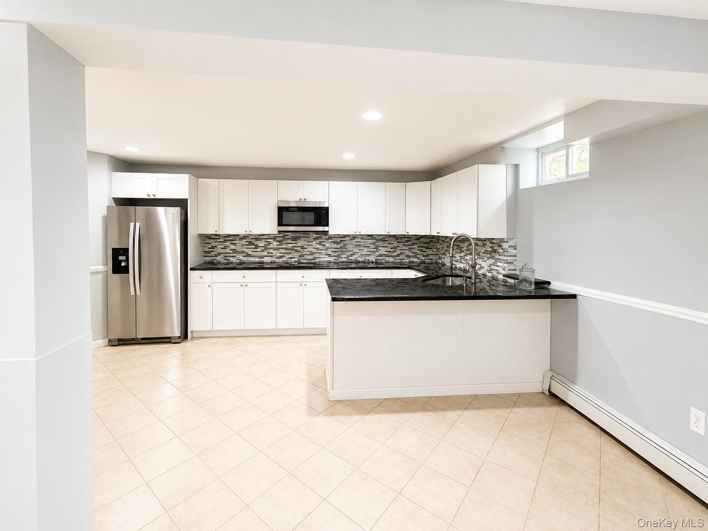 White cabinetry, stainless steel appliances, black countertops, mosaic tile backsplash, and tile flooring