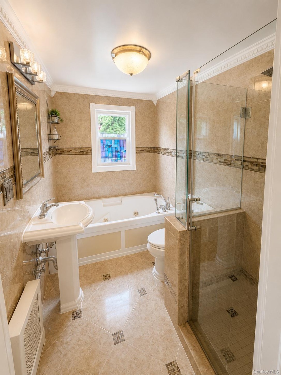 Tiled bathroom featuring a pedestal sink, jetted tub, and a glass-enclosed shower with tiled walls and floor