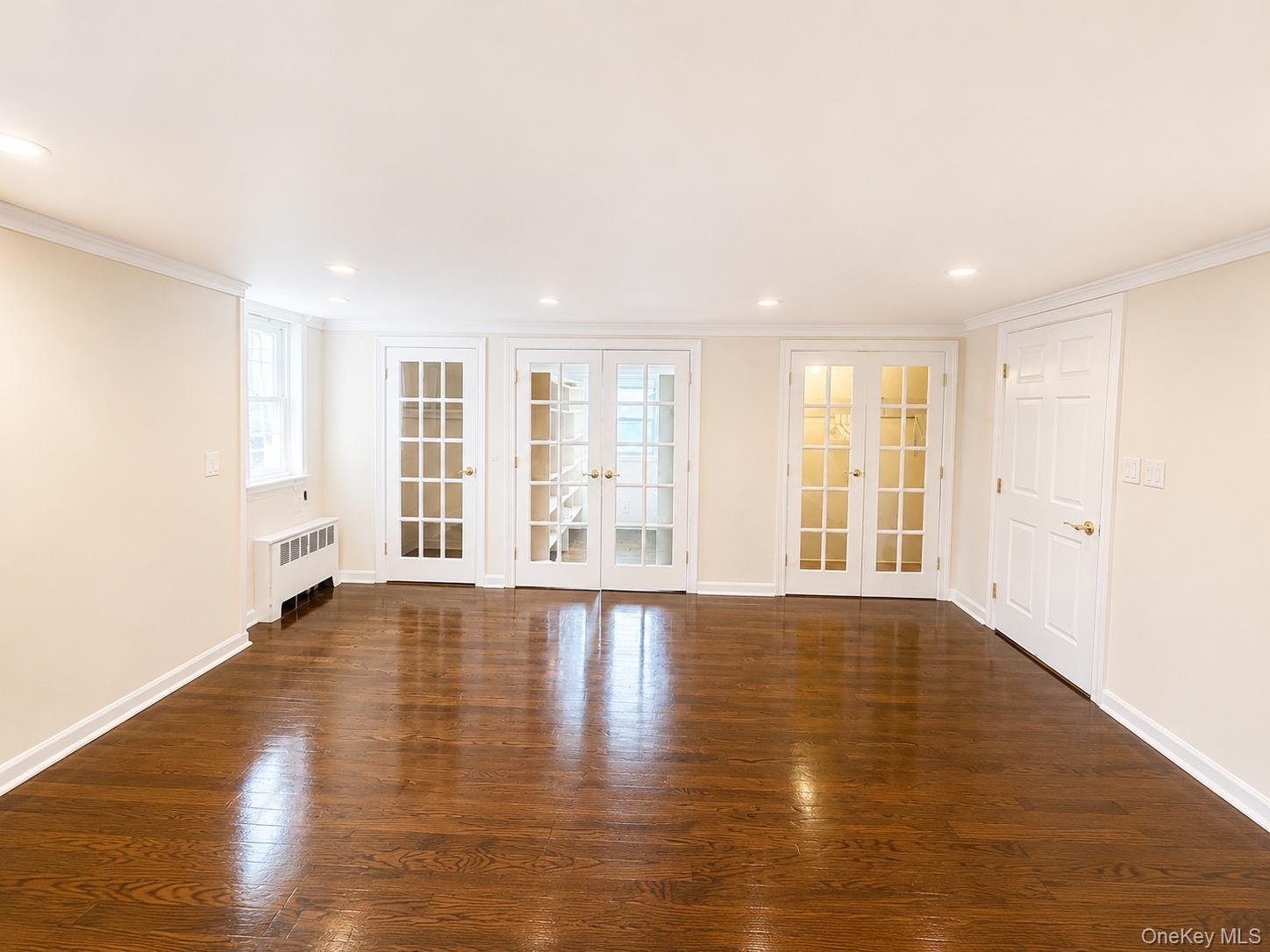 Hardwood flooring, recessed lighting, crown molding, white trim, and a window with a radiator below