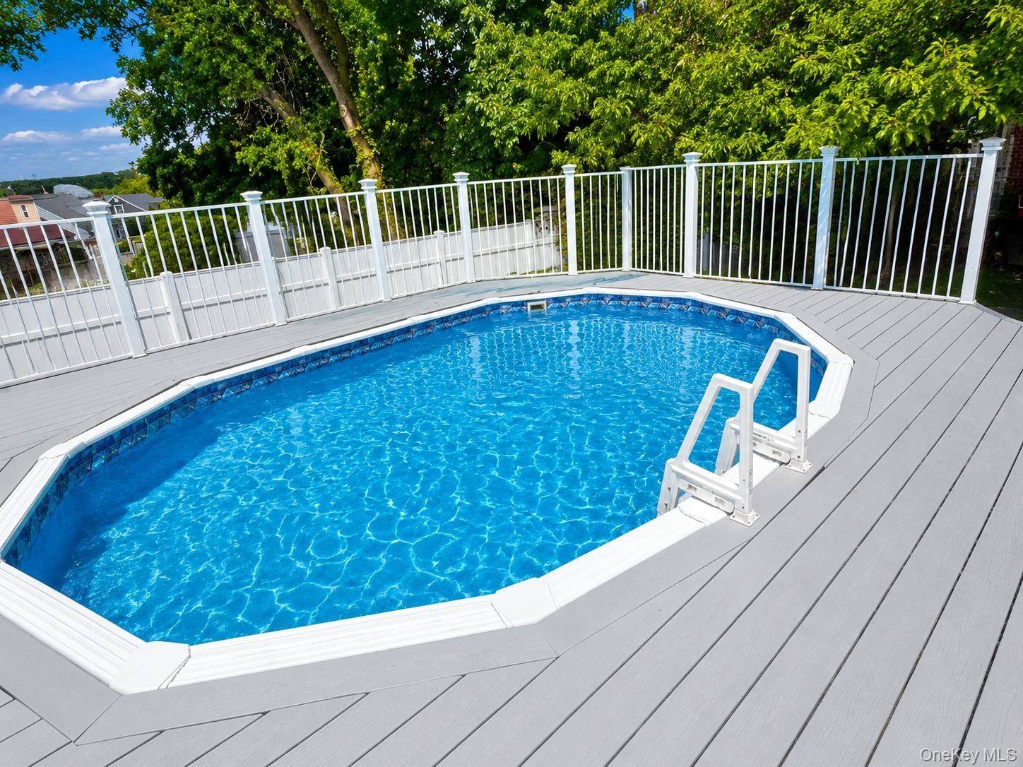 Swimming pool featuring a gray composite deck, perimeter safety fencing, and white entry steps