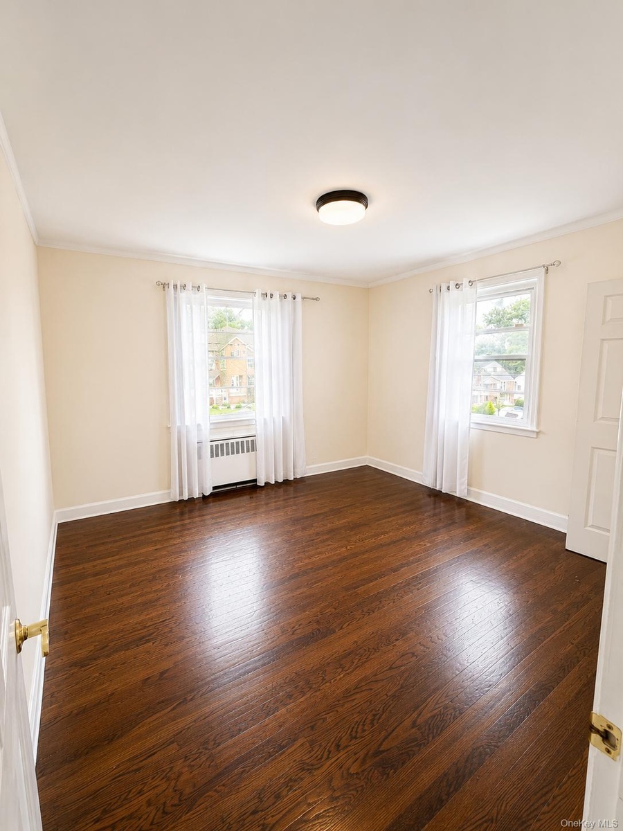 Rich wood-finish flooring, two large windows, white trim, and a contemporary flush-mount ceiling light